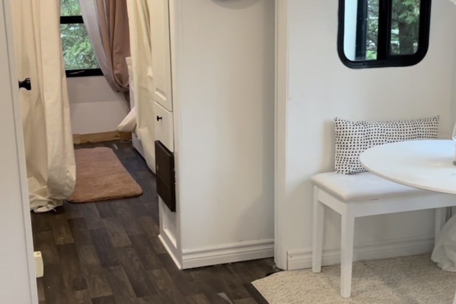 Modern RV rental interior with bright white walls, dark laminate flooring, a cozy dining area, and bedroom entrance.