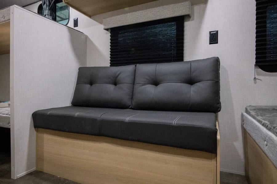 RV rental interior features a versatile dark gray futon-style dinette and bunk beds, offering comfortable living space.