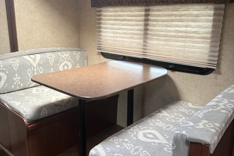 Cozy RV rental dinette featuring a table and two upholstered benches with grey patterned cushions. Ideal for travel.