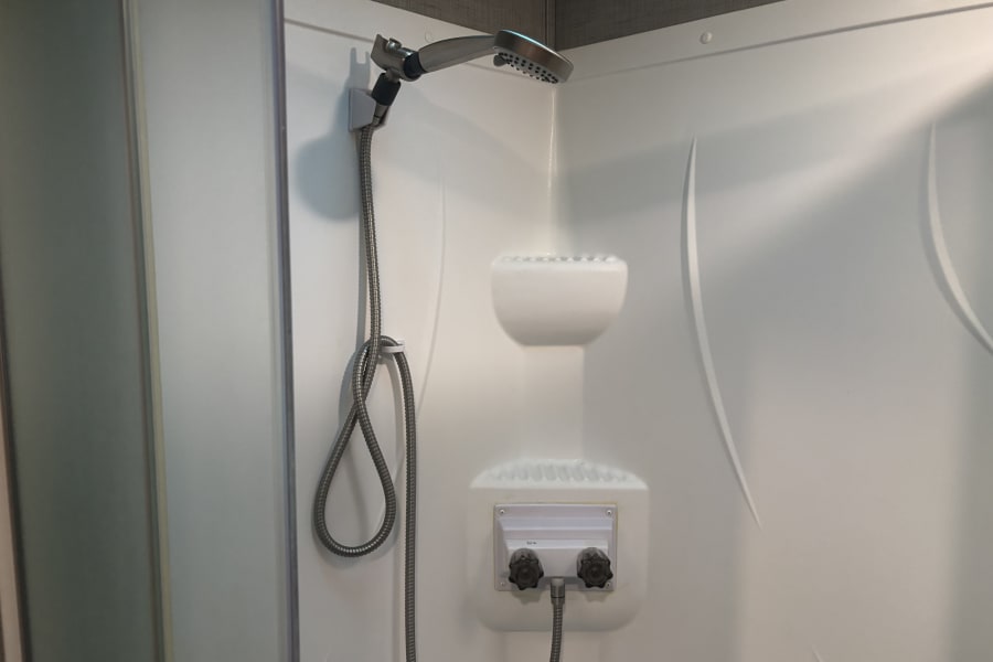 Clean white shower stall with a handheld showerhead and controls, typical for an RV rental bathroom.