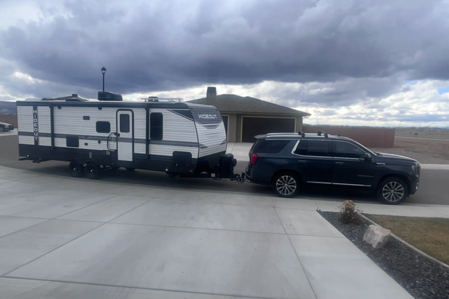 Travel trailer hitched to a dark SUV on a concrete driveway under a cloudy sky. Ready for your next RV rental trip!