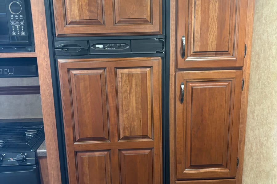 Compact RV rental kitchen featuring a wood-paneled refrigerator, microwave, stove, and pantry cabinets.