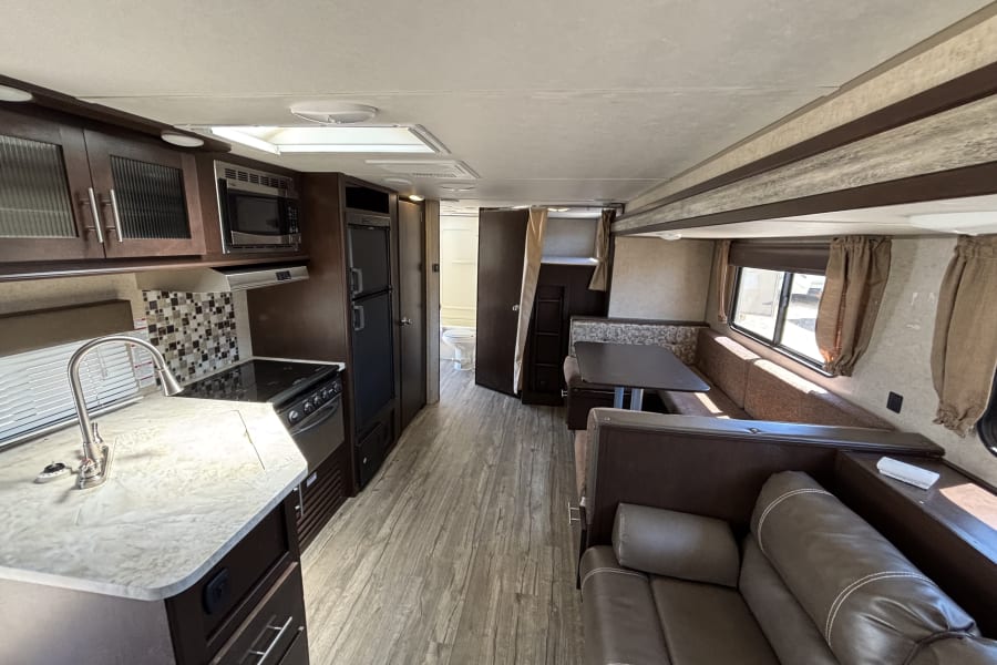Comfortable RV rental interior: modern kitchen, dinette, sofa living area, and bathroom visible down the hall.