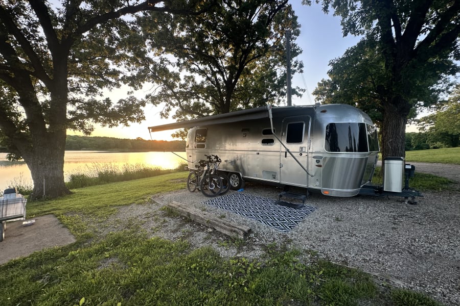 Lakeside Airstream RV rental at sunset, parked with bikes at a serene campsite.