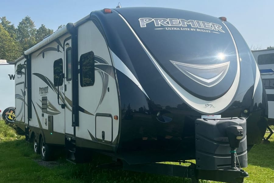 Black & white Premier travel trailer, ideal for an RV rental. Parked on green grass under a sunny, clear sky.