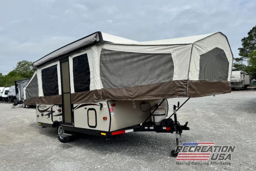 This tan and brown pop-up camper RV rental, fully extended, is parked on a gravel lot, ready for your camping adventure.