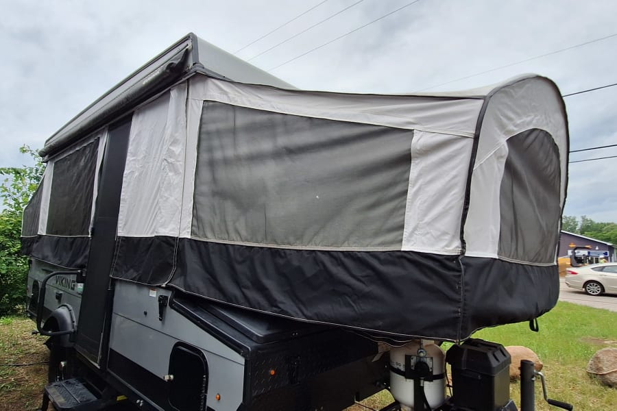 Pop-up camper RV rental fully extended with fabric walls and windows, set up in a grassy outdoor area.