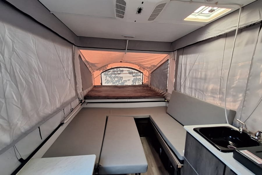 Explore this pop-up RV rental's interior: a cozy bed, convertible dinette, and functional kitchen ready for your journey.