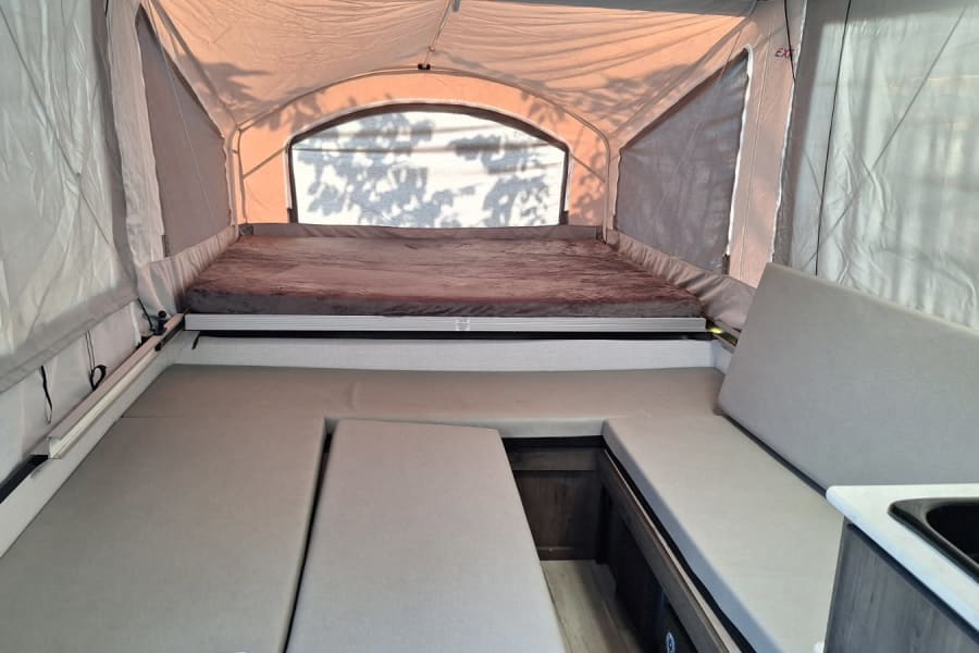 Pop-up camper RV rental interior: bed, dinette, & sink for comfortable camping.