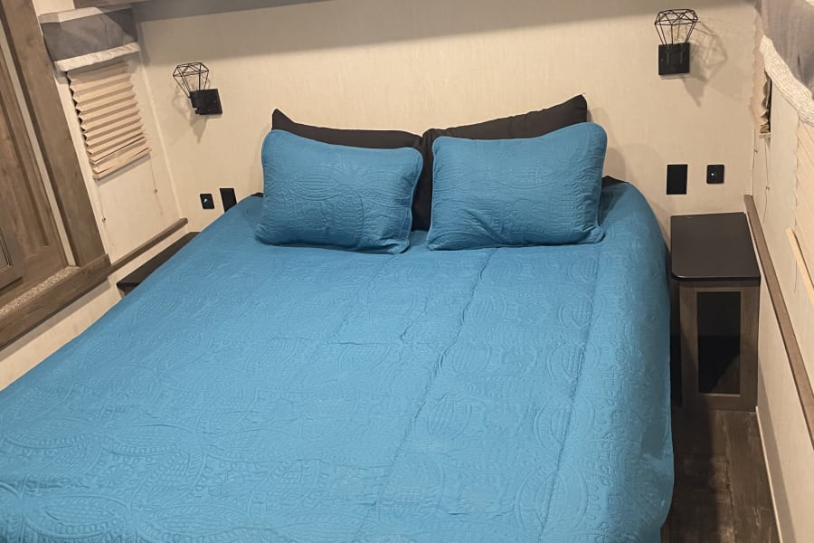 RV rental bedroom with a comfy blue bed, wooden cabinets, and wall sconces for a relaxing journey.