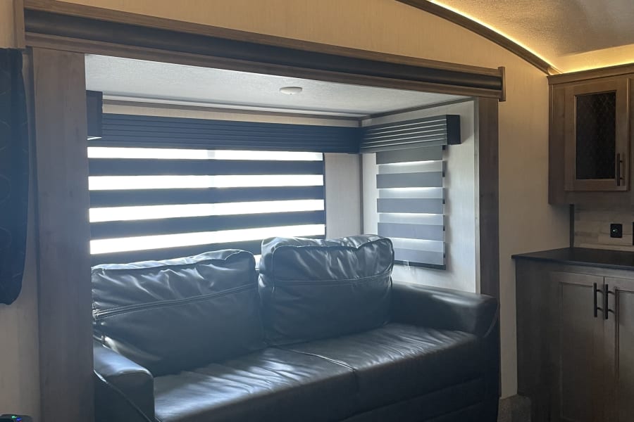 Cozy RV rental interior with a dark leather sofa, modern window blinds, and ambient LED ceiling lighting.