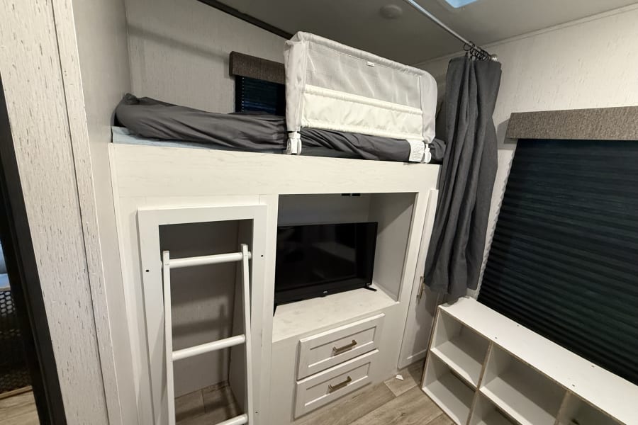Inside an RV rental: bunk beds with a safety rail, ladder, TV, and storage for a comfortable family sleeping area.