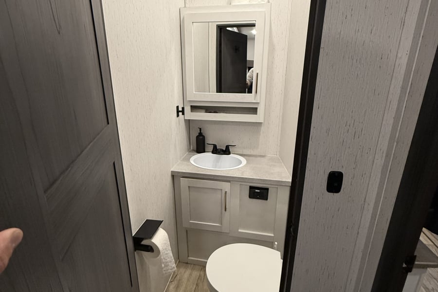 RV rental bathroom: compact, modern design with white toilet, sink, and mirrored cabinet.