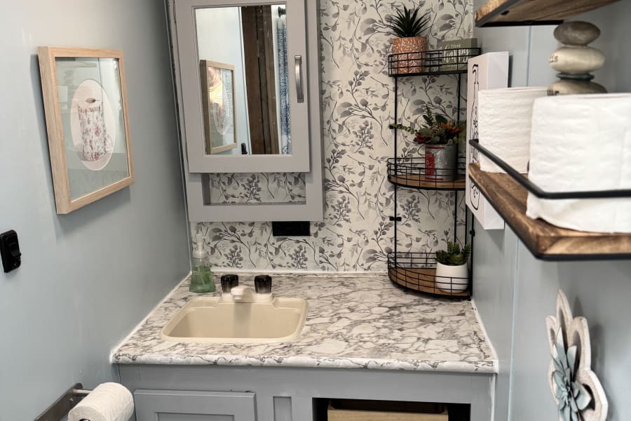 Modern compact RV rental bathroom featuring a vanity, sink, and stylish storage shelves. Perfect for travel comfort.