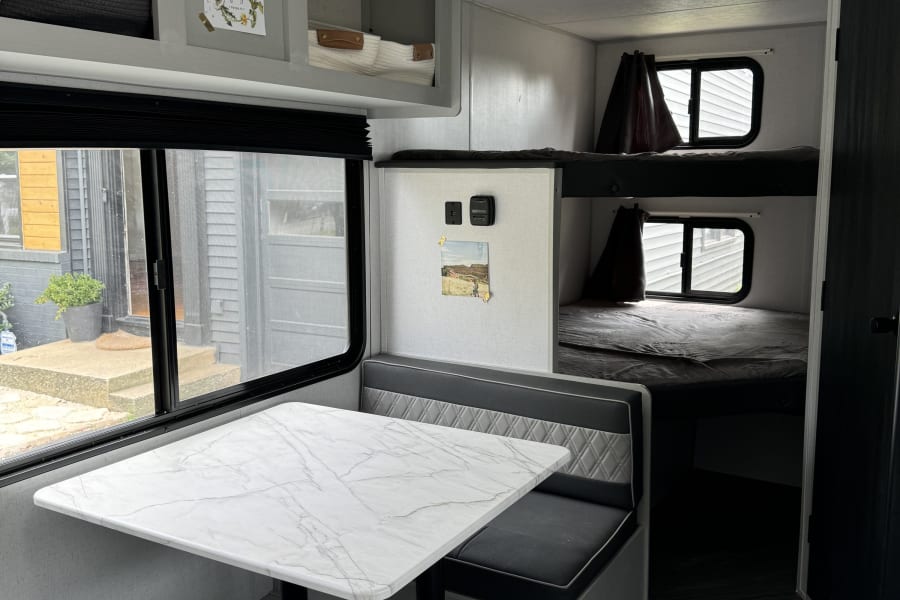 This RV rental showcases a bright dinette area, ample overhead storage, AC unit, and comfortable bunk beds for travel.