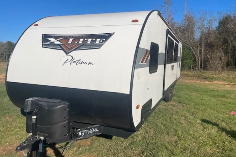 White Wildwood X-Lite Platinum travel trailer, a spacious RV rental, parked on green grass. A bright day for your outdoor escape.