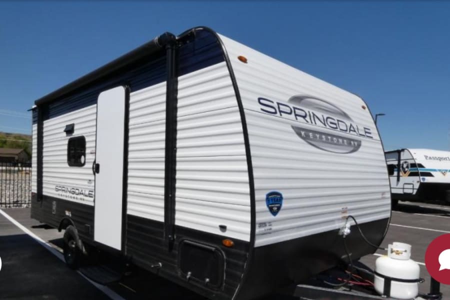 A white Springdale Keystone RV travel trailer, with a propane tank, is parked outside, ideal for an rv rental adventure.