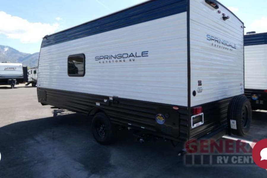 A large white and dark blue Springdale Keystone travel trailer is parked, ready for RV rental. Other RVs are in the background.