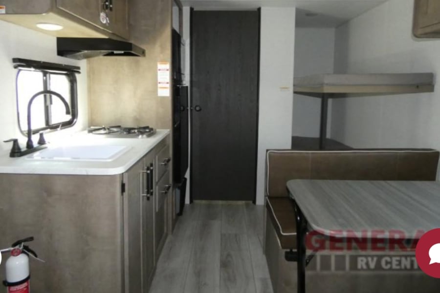 Compact RV rental interior featuring a full kitchen, dinette, and bunk beds for efficient living on the road.