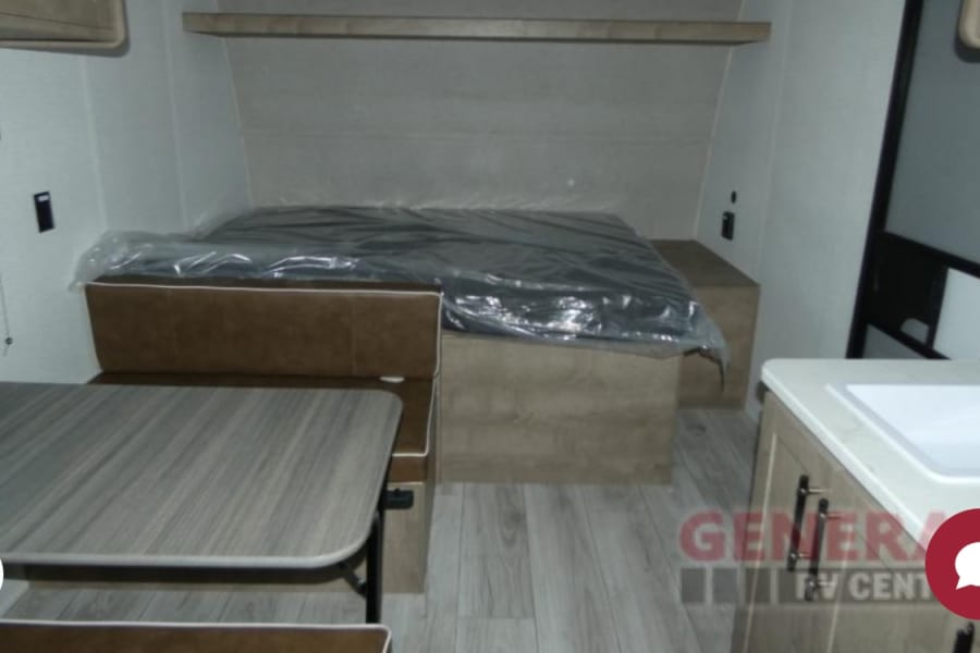Spacious RV rental interior features a cozy bed, convertible dinette, and compact kitchen sink area.