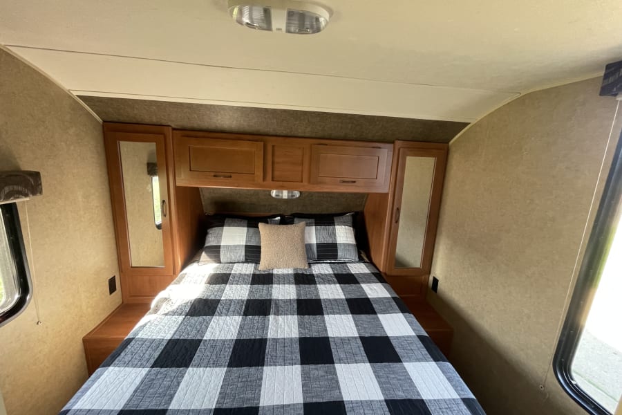 Cozy RV rental bedroom with a black and white checkered comforter, wooden cabinets, and bright window light.