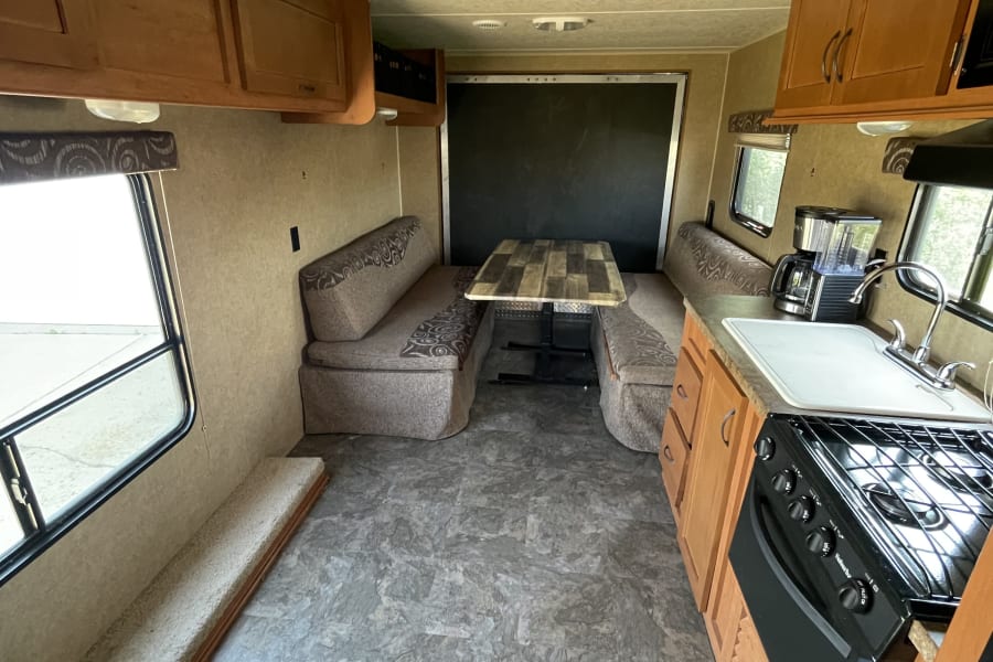 RV rental's interior: a full kitchen with stove and sink, a large U-shaped dinette, and ample floor space. Ready for adventures!