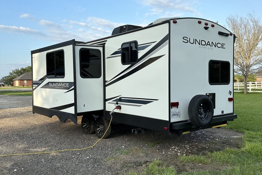 This Sundance Ultra Lite travel trailer RV rental, with slide-outs extended, is parked on gravel, ready for adventure.