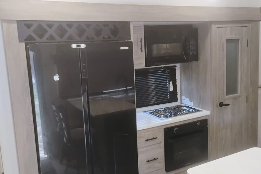 RV rental kitchen: black fridge, microwave, gas stove, oven, wood-grain cabinets. Ideal for travel cooking.
