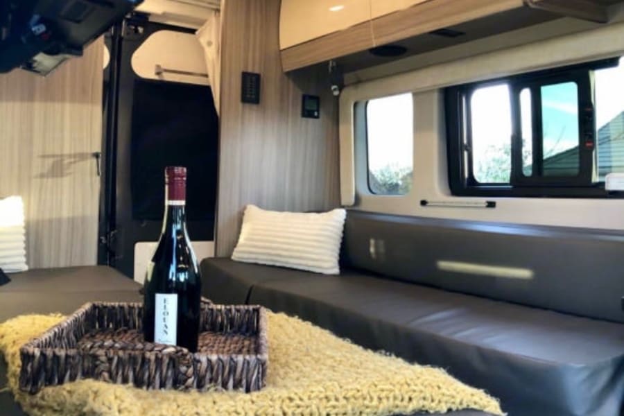 Cozy & modern RV rental interior: comfortable seating, overhead cabinets, and wine bottle in a woven tray. Perfect camper living space.