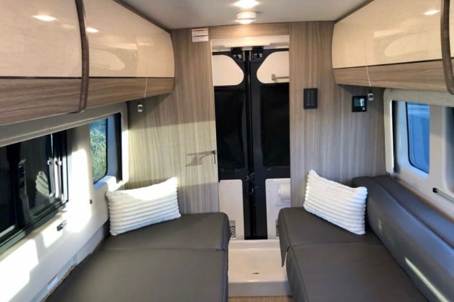 RV rental: Inside a modern camper van with dual beds, overhead cabinets, and bright windows.
