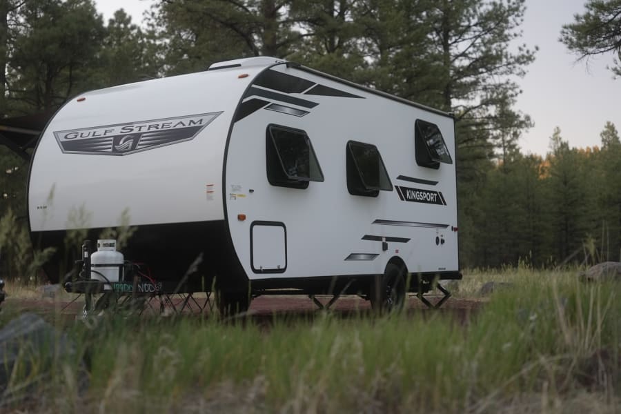 A white Gulf Stream Kingsport RV rental is parked in a serene forest campsite. Ready for adventure and nature.