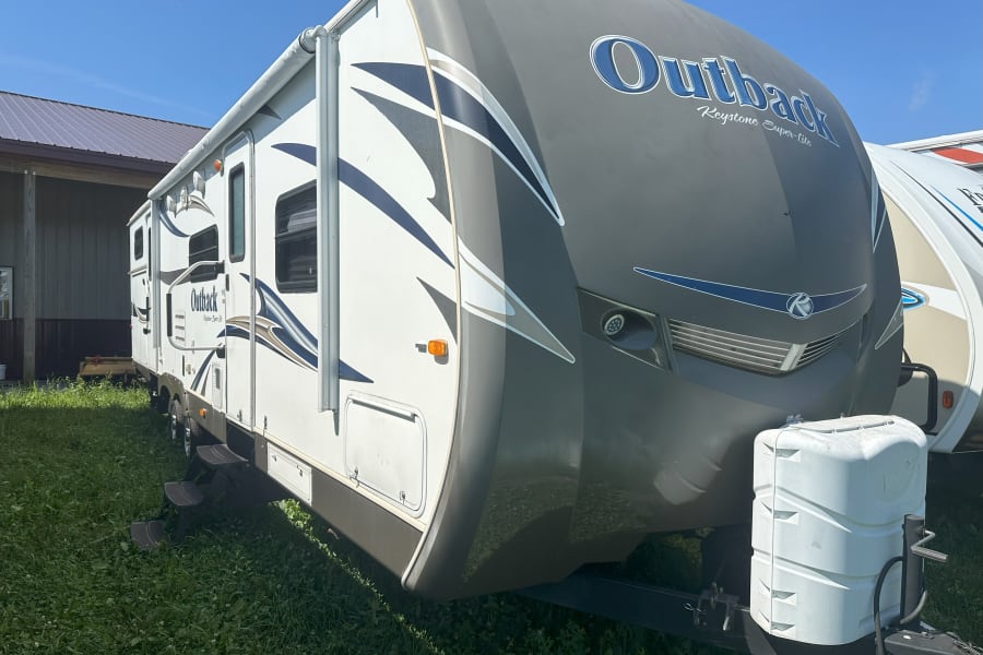 This Outback Keystone travel trailer RV is available for rv rental, parked on grass under a clear sky.