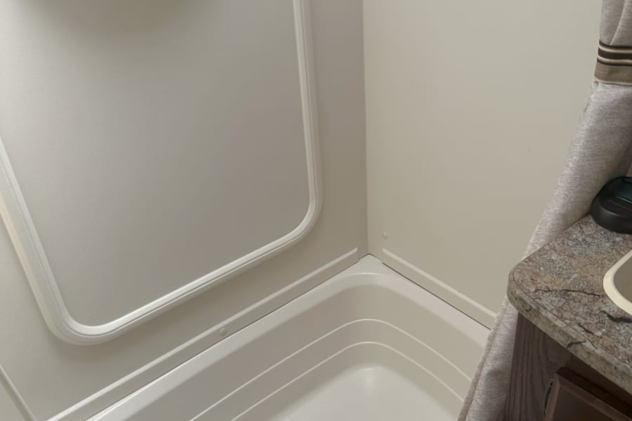 Detailed view of a white, compact RV rental shower with built-in shelf, faucet, and textured floor.