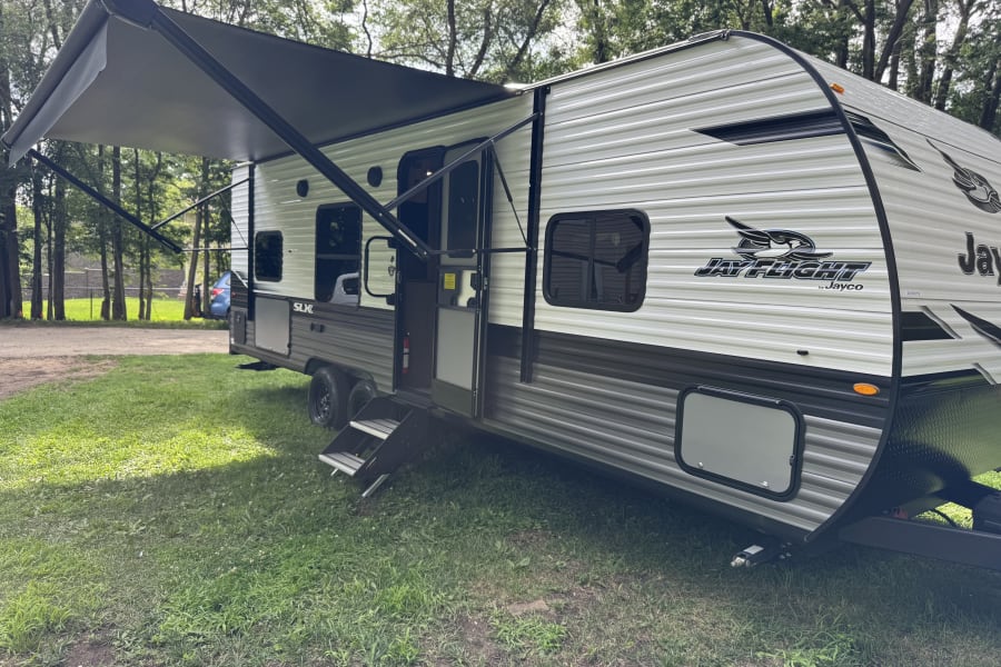 This Jayco RV rental is set up for a sunny outdoor adventure, with its awning extended and steps down, ready for travelers.