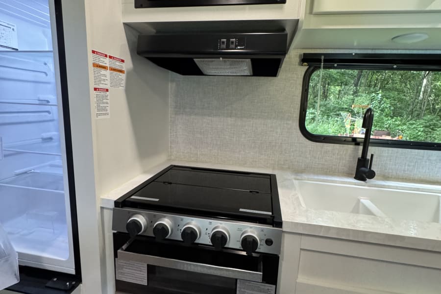 RV rental kitchen with light cabinets, white sink, black microwave/stove, and open refrigerator door.