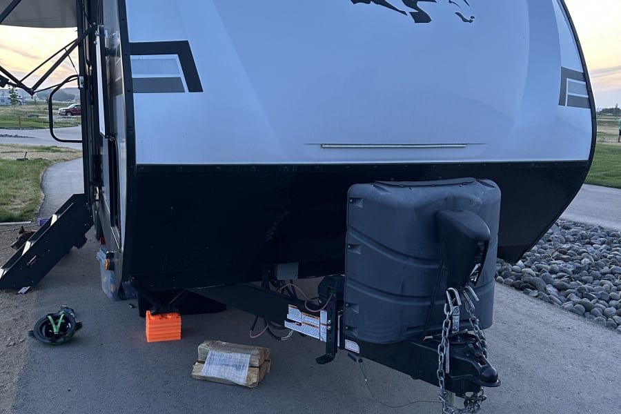 An Open Range travel trailer, ideal for an RV rental, fully set up at a tranquil campsite. Notice leveling blocks & hitch.