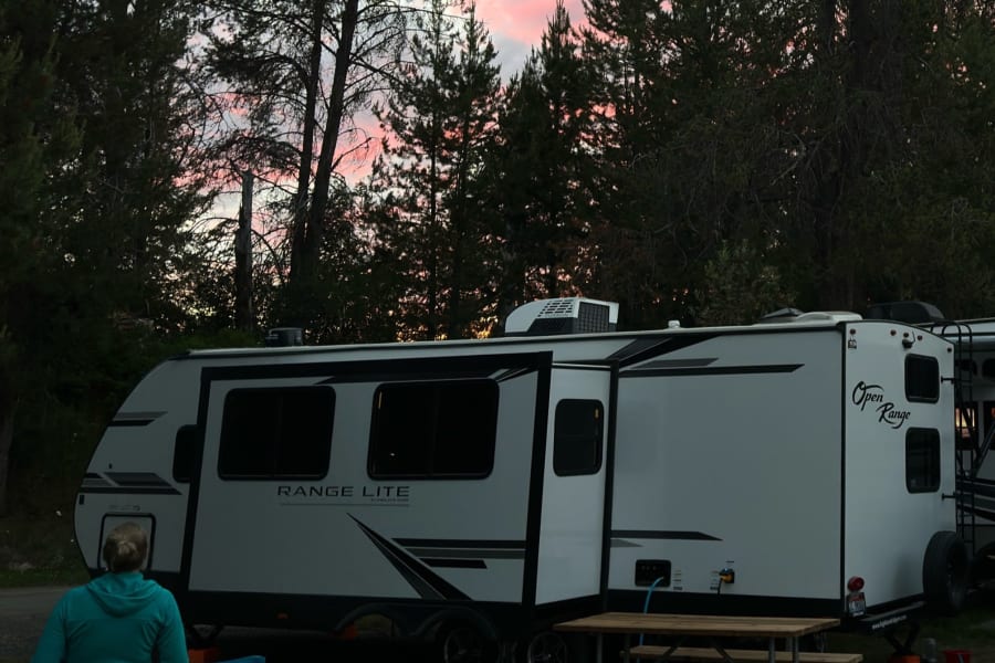 An RV rental offers a peaceful evening: a white travel trailer under a pink sunset, with a picnic table & dogs at camp.