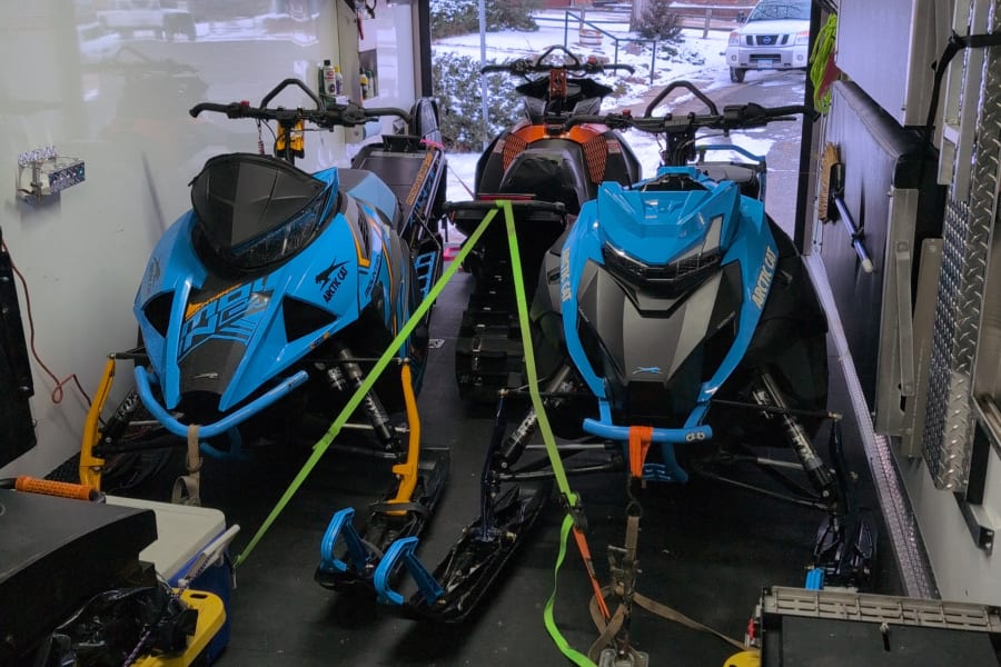 Two Arctic Cat snowmobiles are secured inside a transport trailer, prepared for winter adventures. Perfect for an RV rental trip!