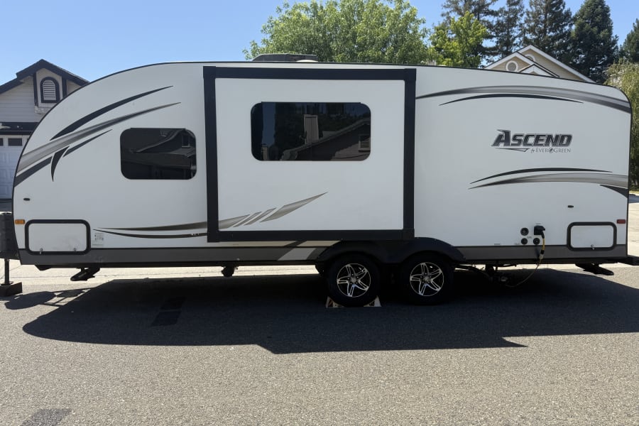 Spacious white travel trailer with slide-out extended, perfect for an RV rental adventure, parked on pavement.