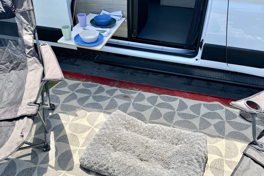 RV rental's outdoor living: pet bed, bowls, pull-out table, and rug create a cozy camp setup outside the van.