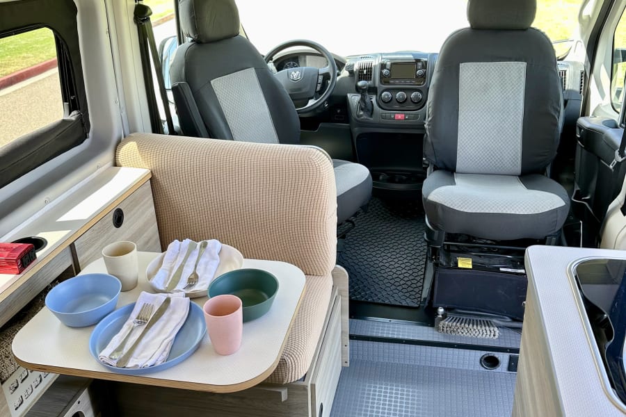 This clean rv rental interior offers a dining table with place settings, comfortable seating, and the full cockpit view.