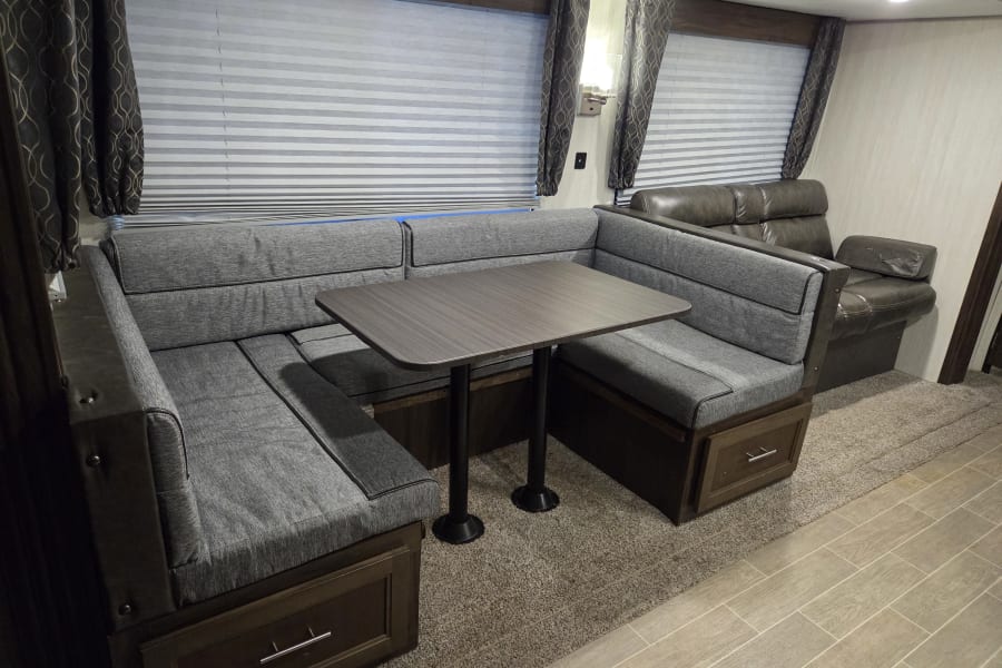 RV rental interior featuring a modern dinette with U-shaped booth seating, table, and comfortable recliner sofa.