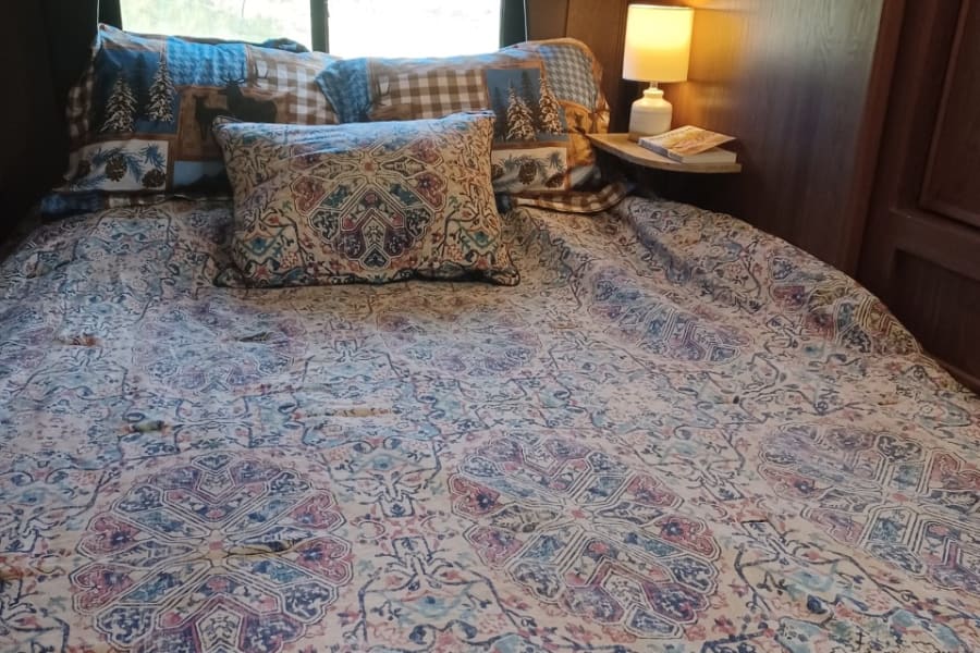 Cozy RV rental bedroom with patterned bedding, a window view, and reading lamp.