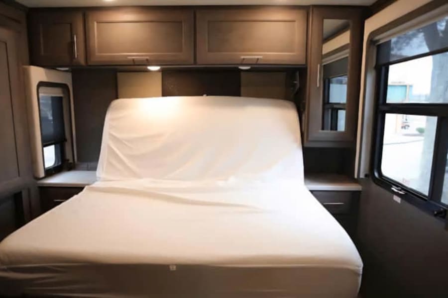 Comfortable RV rental bedroom with a neatly made bed, overhead storage, and natural light from the windows.