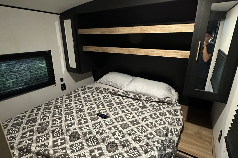 RV rental bedroom featuring a patterned bed, storage shelves, and mirrored wardrobe, showing a cozy and functional space.