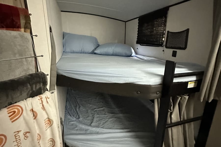 RV rental bunk beds with blue sheets and pillows, a ladder, and wall storage, offering cozy sleeping space.