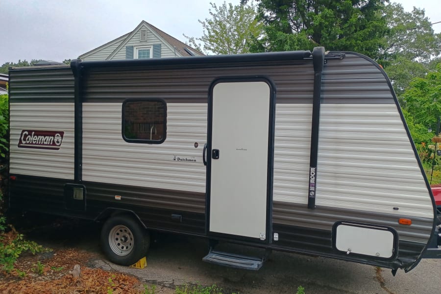 A grey and white Coleman Dutchmen travel trailer, perfect for an RV rental, is parked outdoors.