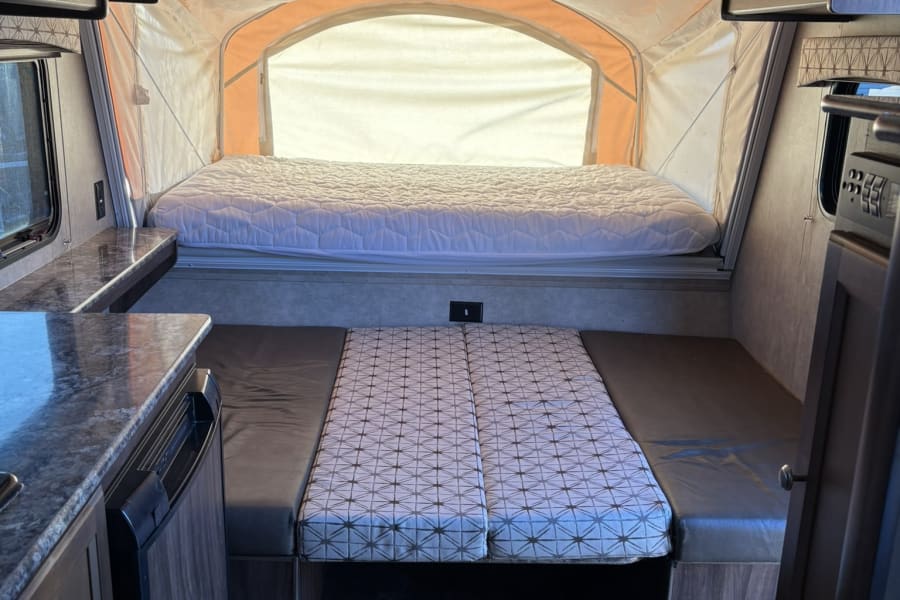 This rv rental interior features a pop-out bed, dinette, and compact kitchen with overhead cabinets.