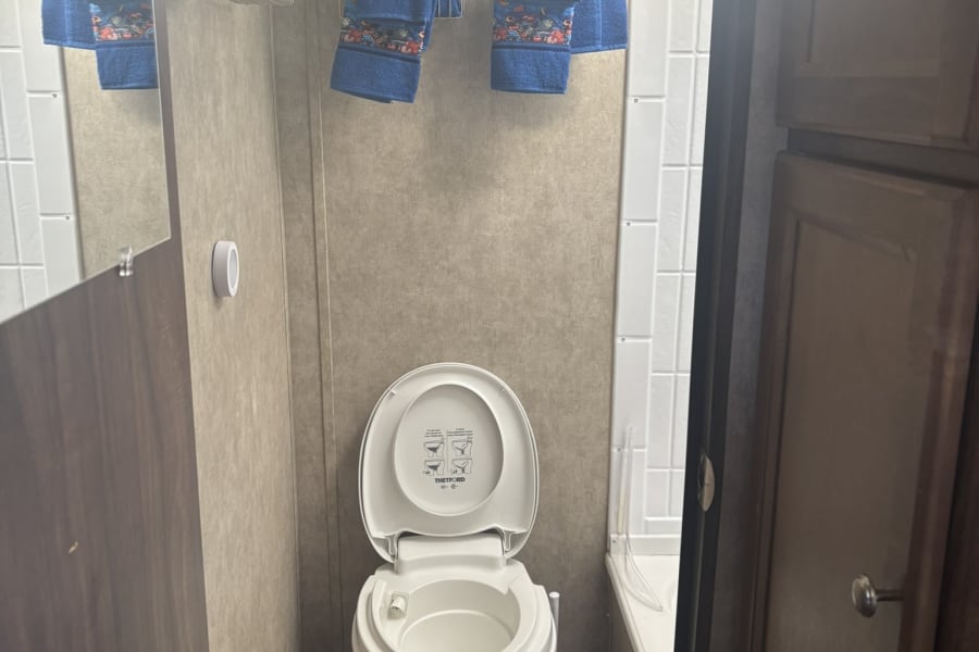 Compact RV rental bathroom with white toilet, small shower/tub, and patterned blue towels on wall racks.