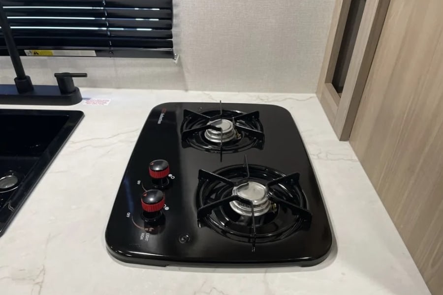 RV rental kitchen: compact black two-burner gas stove, sink, and light marble-patterned countertop. Perfect for road trips.